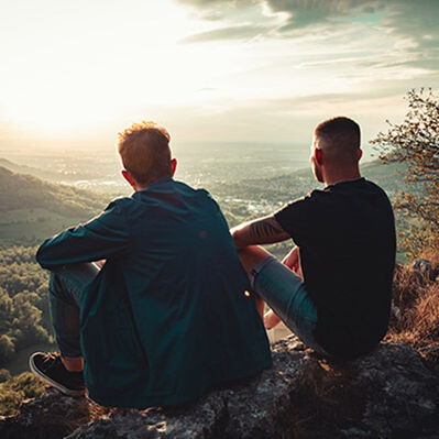 Zwei Freunde sitzen auf einem Fels und schauen ins Tal 