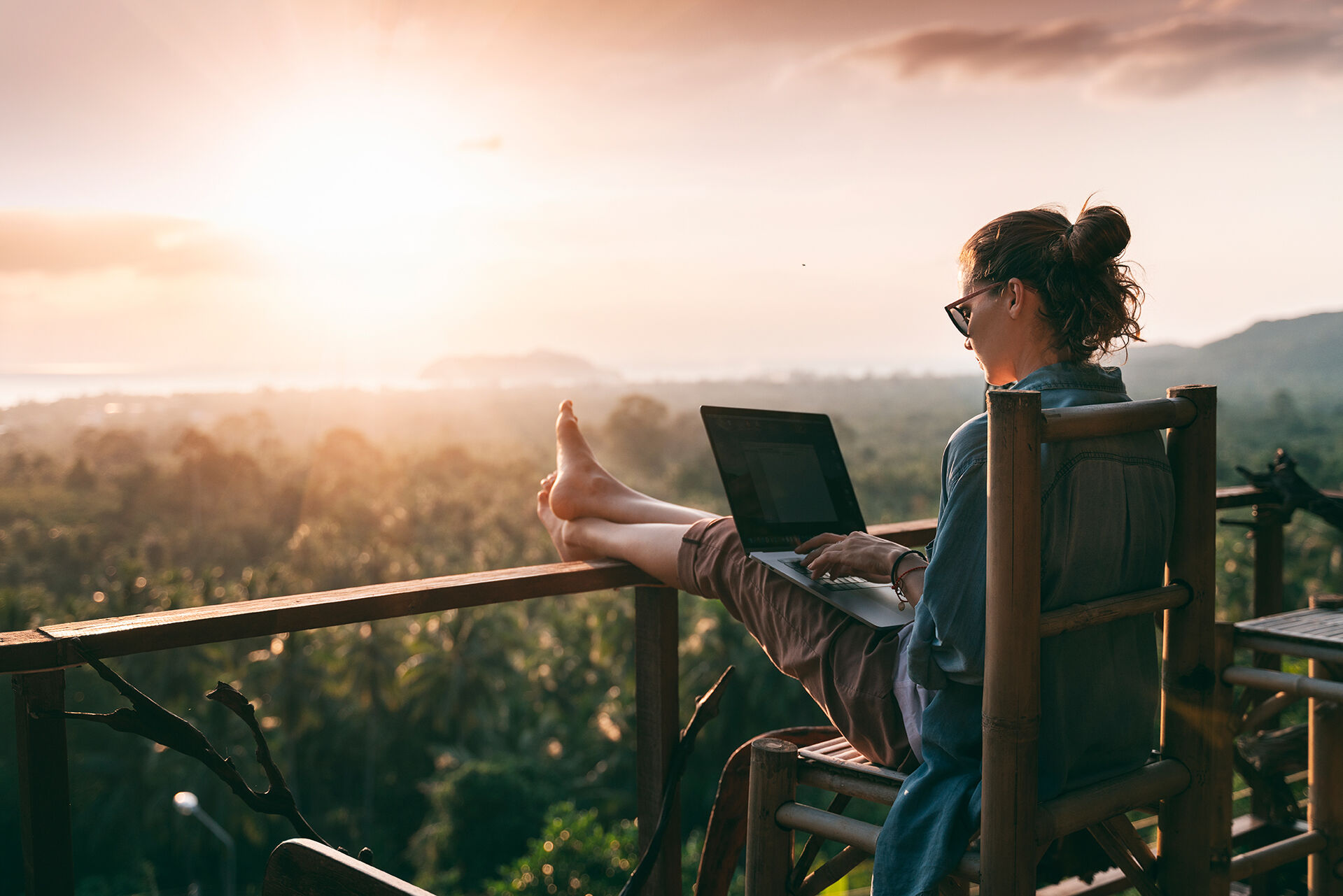 Junge Frau arbeitet am Laptop bei Sonnenaufgang auf der Spitze eines Berges 